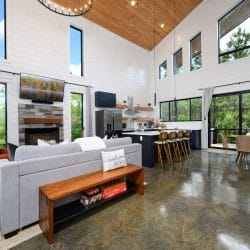Open living area under a vaulted ceiling with a gray sofa and wood bench, the kitchen and dining table behind